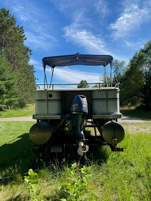 Rear view of an olive green vintage truck with open cargo bed and canopy parked on grass surrounded by trees