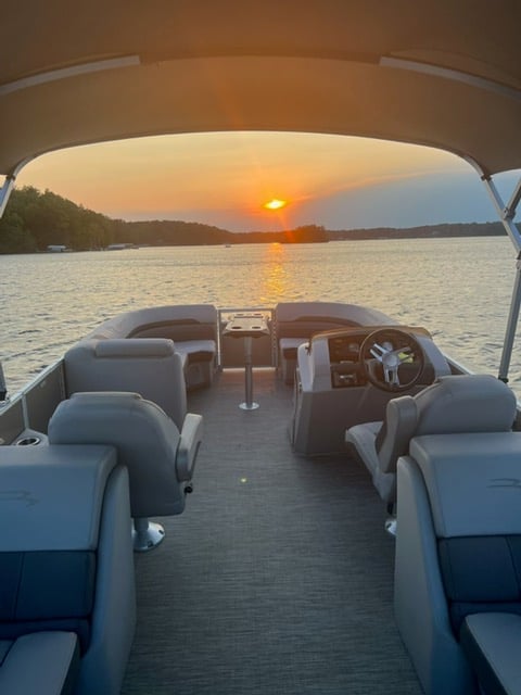 View from inside a boat facing the steering wheel, with sunset over calm water and forested shoreline