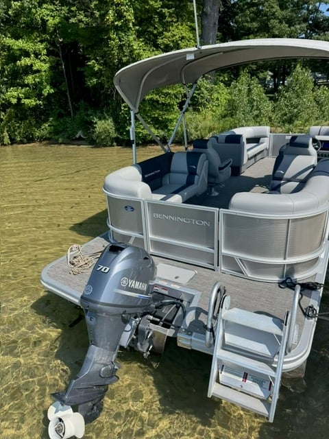 Bennington pontoon boat with gray and white seating, Yamaha outboard motor, and bimini top on calm green water surrounded by trees