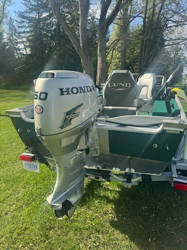 Green and white fishing boat with Honda 50hp outboard motor mounted on trailer in grass with trees in background