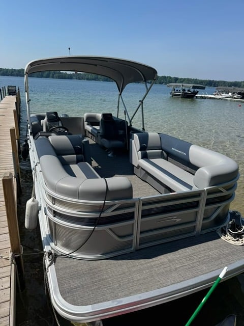 White and black pontoon boat with canopy docked at wooden pier on calm blue water