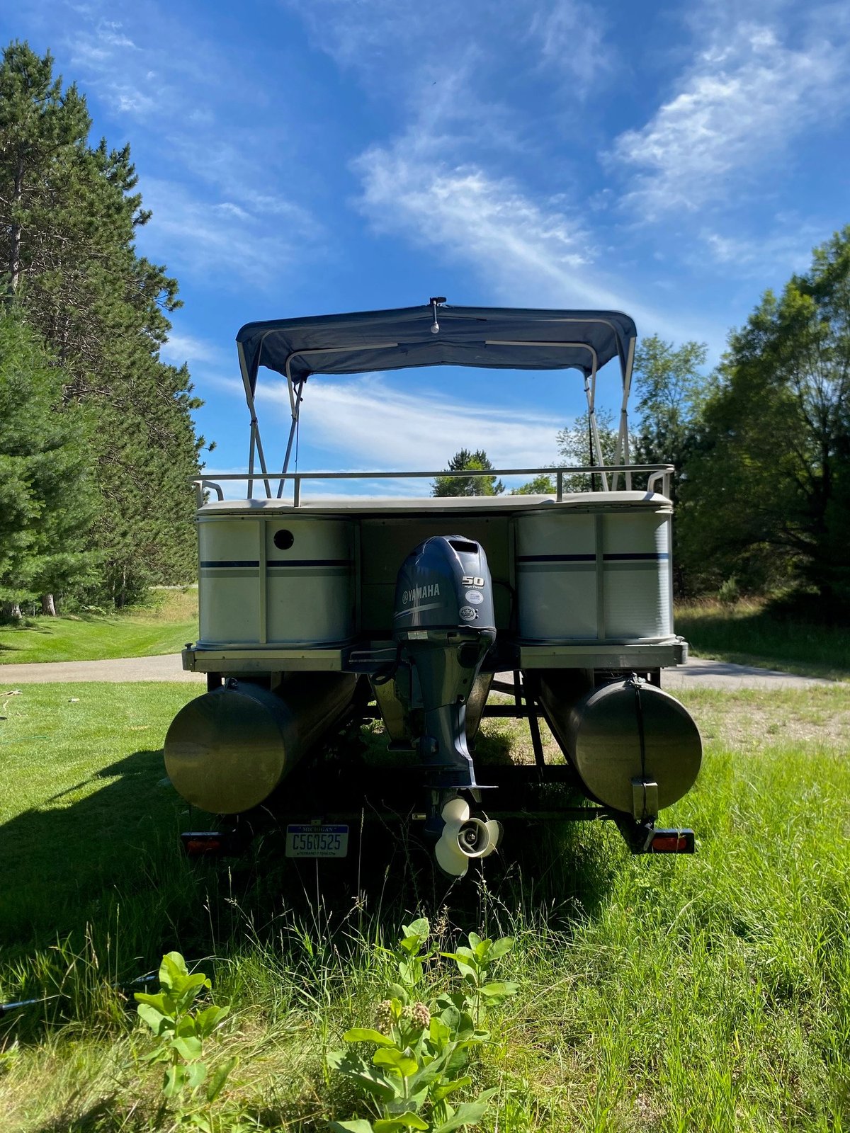 Rear view of vintage olive-green military truck with canvas canopy parked on grass with trees and blue sky in background