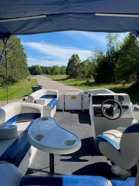 Interior view of a blue and white pontoon boat on a scenic country road lined with trees under a clear sky